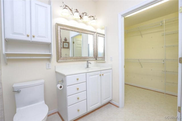 bathroom with vanity, baseboards, toilet, and a walk in closet