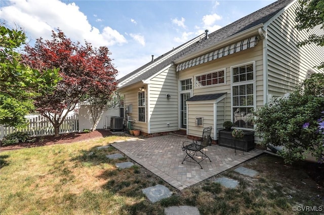 rear view of property featuring fence, a shingled roof, a patio area, a lawn, and central air condition unit