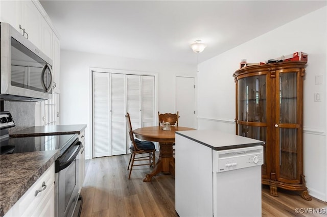 kitchen featuring wood finished floors, stainless steel appliances, dark countertops, white cabinetry, and a center island