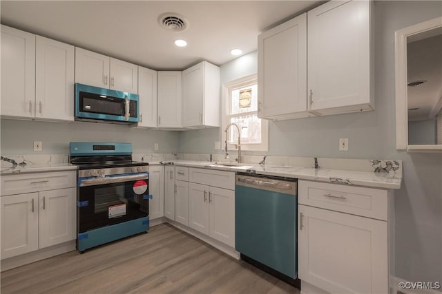 kitchen with light wood finished floors, a sink, stainless steel appliances, visible vents, and white cabinetry