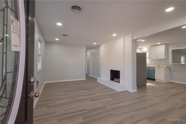 unfurnished living room featuring baseboards, visible vents, wood finished floors, and a brick fireplace