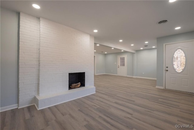 unfurnished living room featuring recessed lighting, a brick fireplace, visible vents, baseboards, and wood finished floors