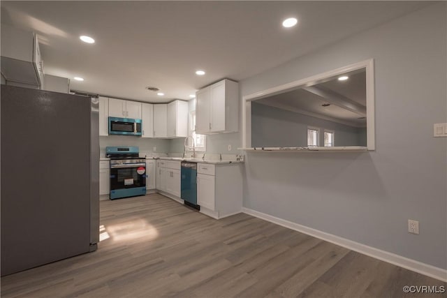 kitchen with light wood-style flooring, white cabinets, stainless steel appliances, light countertops, and baseboards