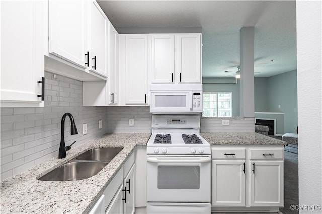 kitchen with white appliances, a sink, ceiling fan, white cabinetry, and backsplash