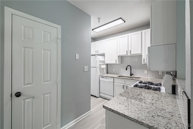 kitchen featuring a sink, white appliances, decorative backsplash, white cabinetry, and light wood-type flooring