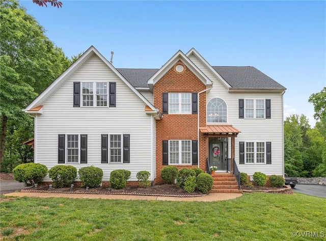 view of front of home featuring a front lawn, a shingled roof, and brick siding