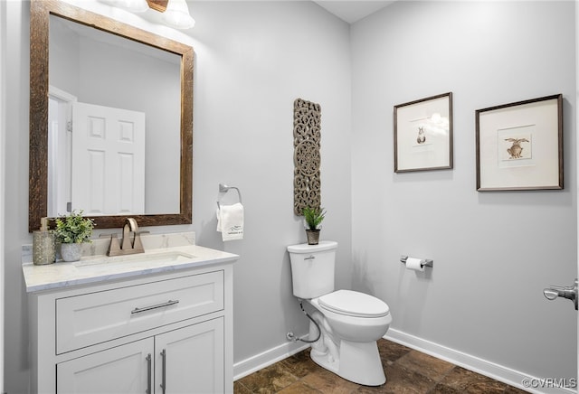 bathroom featuring baseboards, toilet, vanity, and stone finish floors