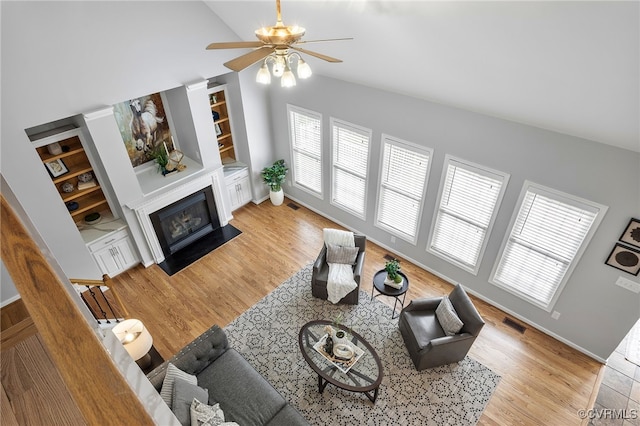 living area featuring vaulted ceiling, ceiling fan, plenty of natural light, a fireplace with flush hearth, and built in features