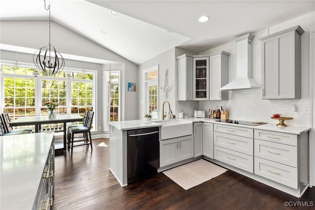 kitchen with a peninsula, light countertops, wall chimney exhaust hood, a sink, and dishwasher