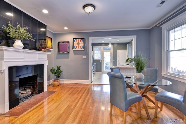 dining area with light wood finished floors, baseboards, a tiled fireplace, and plenty of natural light