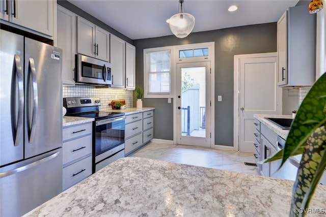 kitchen featuring stainless steel appliances, tasteful backsplash, marble finish floor, light stone counters, and gray cabinetry