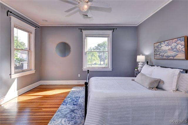 bedroom with ornamental molding, multiple windows, wood finished floors, and baseboards