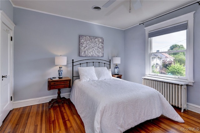 bedroom with visible vents, radiator heating unit, baseboards, ornamental molding, and wood finished floors
