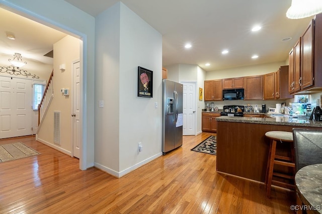 kitchen featuring light wood-style floors, black appliances, a sink, visible vents, and a peninsula