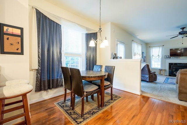 dining area featuring baseboards, wood finished floors, ceiling fan with notable chandelier, and a glass covered fireplace