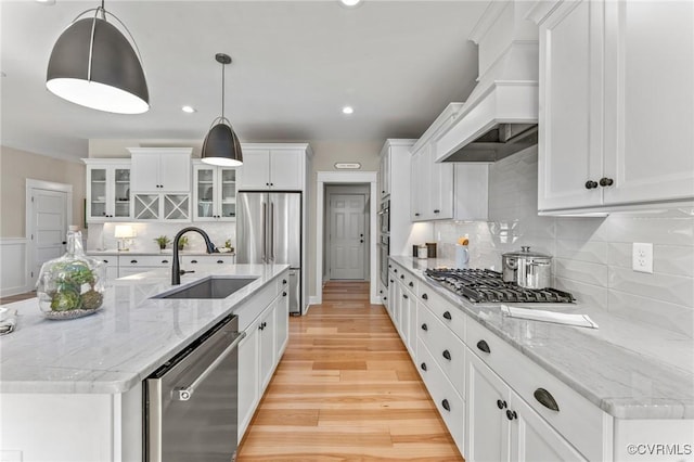 kitchen featuring glass insert cabinets, custom range hood, appliances with stainless steel finishes, a sink, and white cabinetry