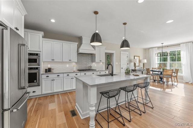 kitchen featuring appliances with stainless steel finishes, a sink, white cabinetry, visible vents, and premium range hood