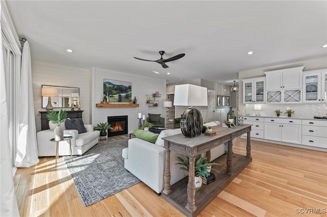 living room with recessed lighting, a ceiling fan, light wood-style floors, and a glass covered fireplace