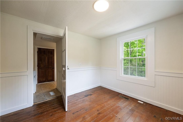 empty room with a wainscoted wall, hardwood / wood-style floors, and visible vents