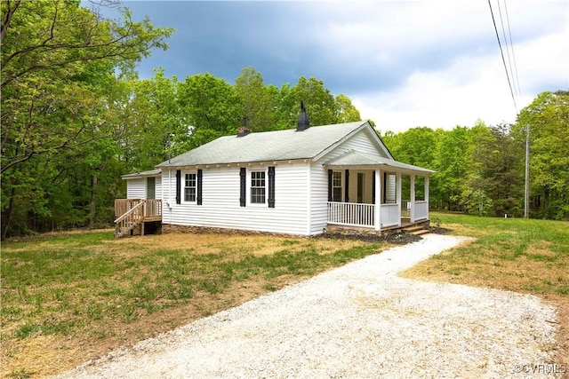 view of front of home featuring driveway, a wooded view, a shingled roof, covered porch, and a front lawn