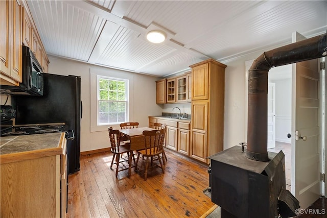 kitchen with light wood finished floors, a sink, glass insert cabinets, black appliances, and baseboards
