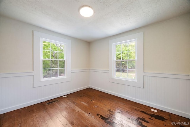 empty room featuring visible vents, a wainscoted wall, a healthy amount of sunlight, and wood-type flooring
