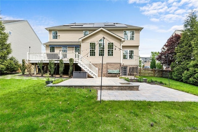 back of property featuring a lawn, a wooden deck, roof mounted solar panels, and a patio area