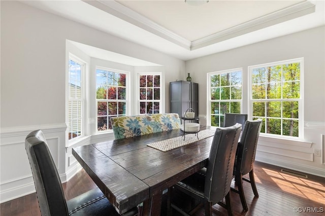 dining area with wood-type flooring, a tray ceiling, a wainscoted wall, visible vents, and ornamental molding