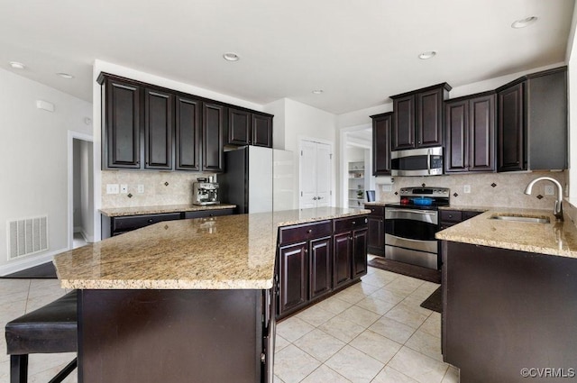 kitchen featuring light stone countertops, stainless steel appliances, a center island, a sink, and visible vents