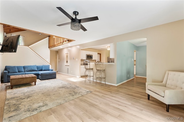 living room with stairway, ceiling fan, baseboards, and light wood finished floors