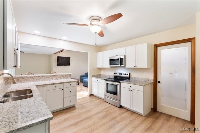 kitchen featuring a sink, light wood finished floors, stainless steel appliances, a ceiling fan, and a peninsula