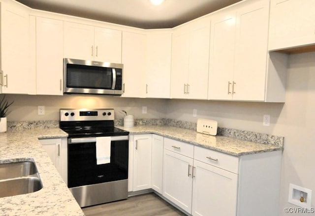 kitchen featuring white cabinets, a sink, light wood-style floors, stainless steel appliances, and light stone countertops
