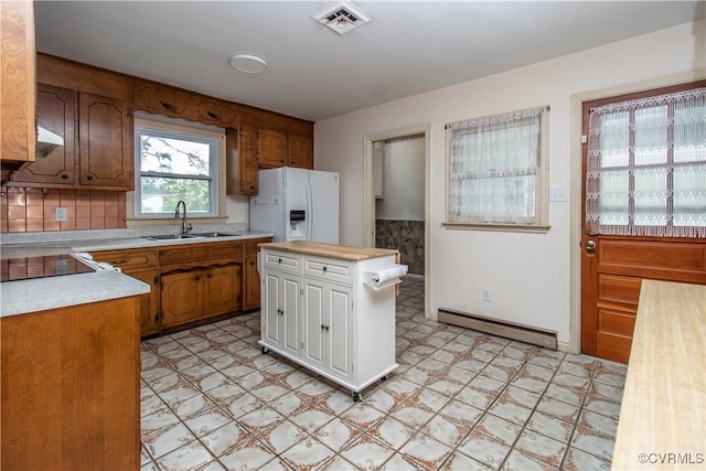 kitchen featuring baseboard heating, white refrigerator with ice dispenser, a sink, light flooring, and tasteful backsplash