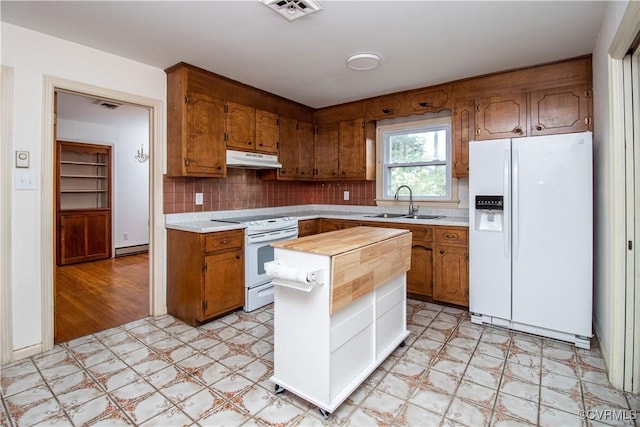 kitchen featuring white appliances, light flooring, under cabinet range hood, and brown cabinets
