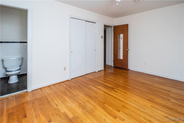 unfurnished bedroom featuring light wood-type flooring, ensuite bathroom, tile walls, and baseboards