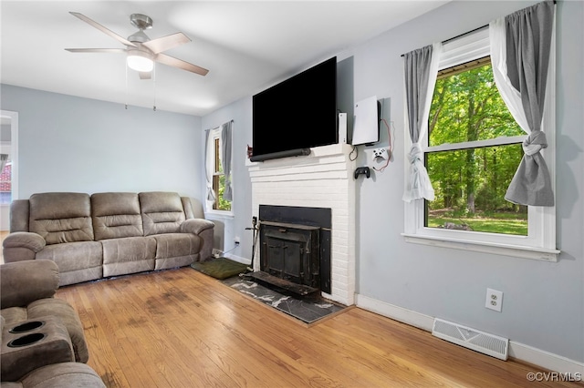 living room featuring wood finished floors, ceiling fan, a brick fireplace, and baseboards