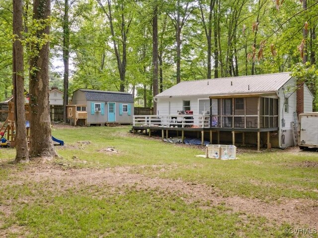 rear view of house featuring metal roof, a lawn, a deck, a sunroom, and an outdoor structure