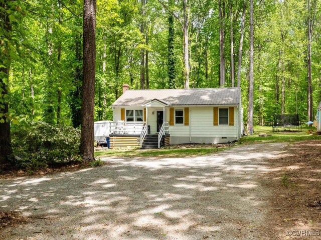 single story home featuring covered porch, a chimney, crawl space, a view of trees, and driveway