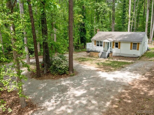 view of front of property with a chimney, dirt driveway, crawl space, a porch, and a wooded view