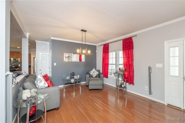 living area featuring light wood-style floors, a notable chandelier, crown molding, visible vents, and baseboards