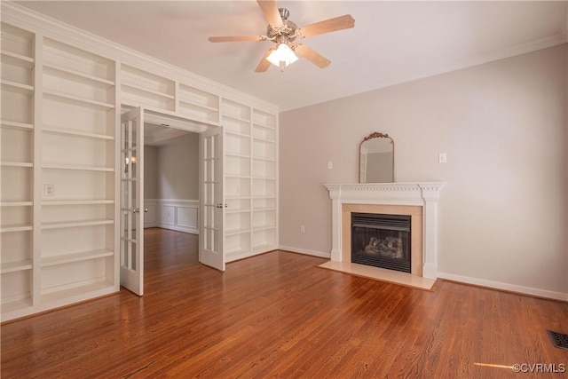 unfurnished living room featuring french doors, wood finished floors, built in features, ceiling fan, and a fireplace with flush hearth