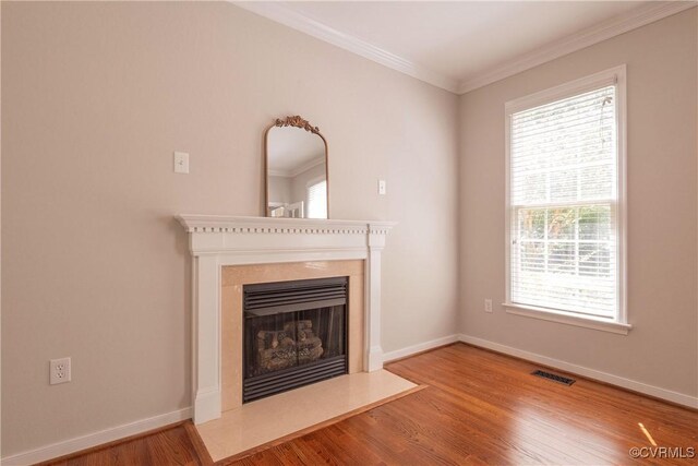 unfurnished living room featuring plenty of natural light, visible vents, a fireplace with flush hearth, crown molding, and wood finished floors