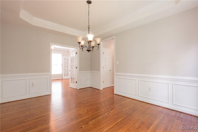 spare room with a decorative wall, wood finished floors, a chandelier, crown molding, and wainscoting