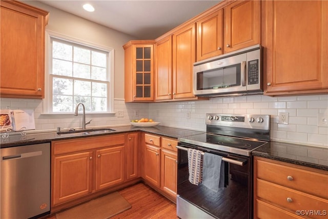 kitchen featuring light wood-type flooring, dark stone countertops, appliances with stainless steel finishes, and a sink