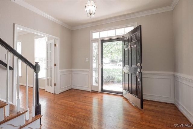 entryway featuring stairs, ornamental molding, a wainscoted wall, and wood finished floors