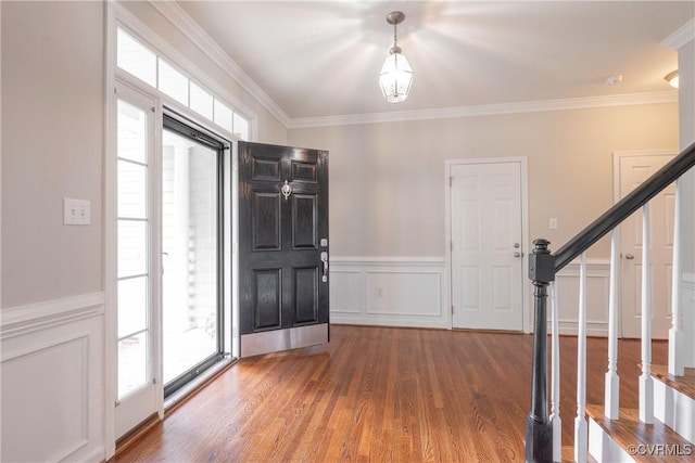 entryway featuring stairs, a decorative wall, crown molding, and wood finished floors