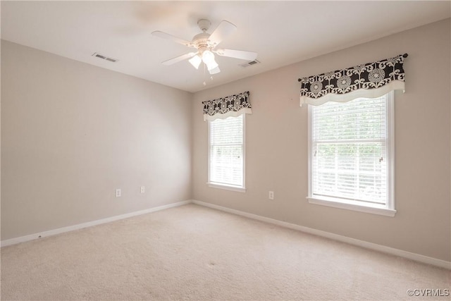 carpeted spare room with baseboards, ceiling fan, and visible vents