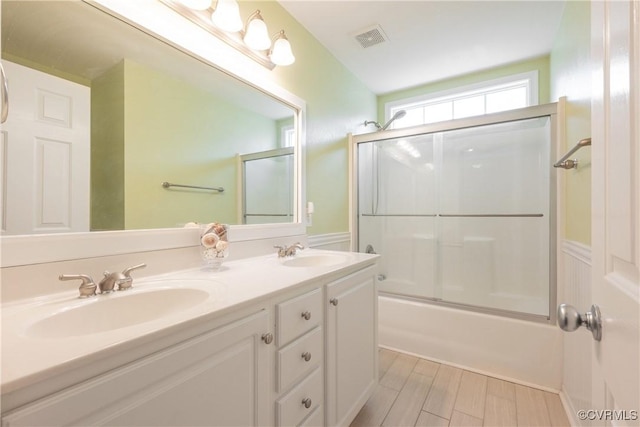 bathroom with a sink, double vanity, shower / bath combination with glass door, and visible vents