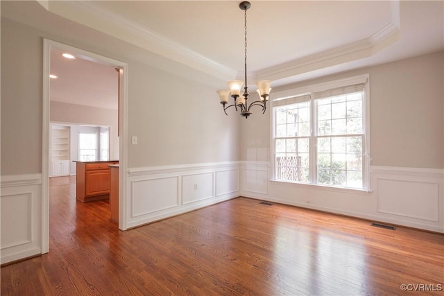 empty room featuring an inviting chandelier, a decorative wall, wainscoting, and a raised ceiling