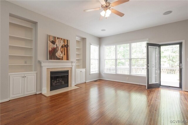 unfurnished living room featuring a fireplace with flush hearth, built in features, baseboards, ceiling fan, and hardwood / wood-style flooring